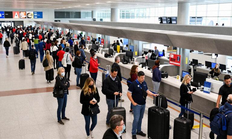 Crowded airport check-in area with passengers queuing at counters and airline staff behind the desks.