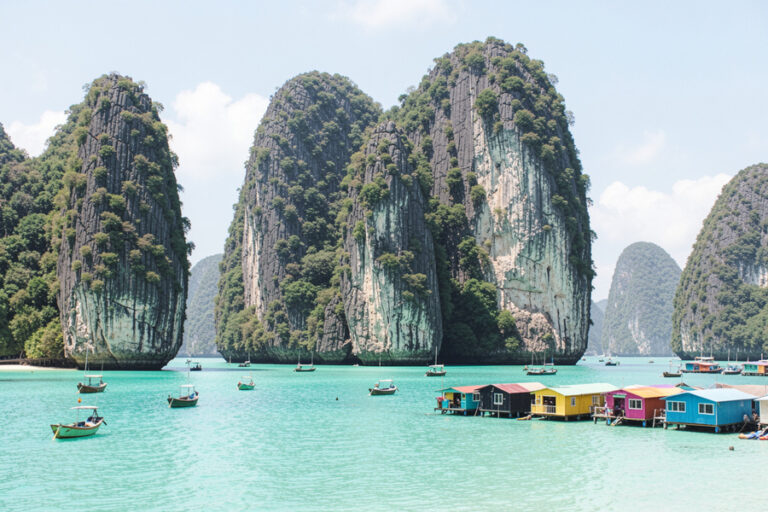 Turquoise water with towering limestone islands and colorful floating houses, with small boats nearby.