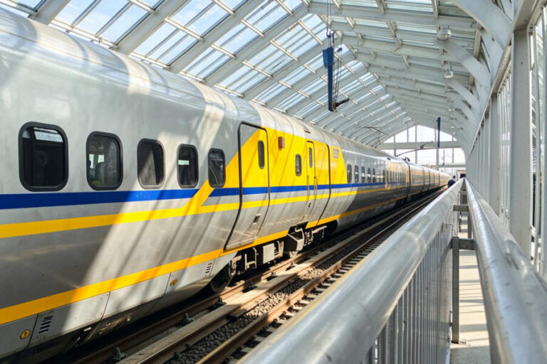 Silver passenger train with yellow and blue stripes at a glass-covered station platform.