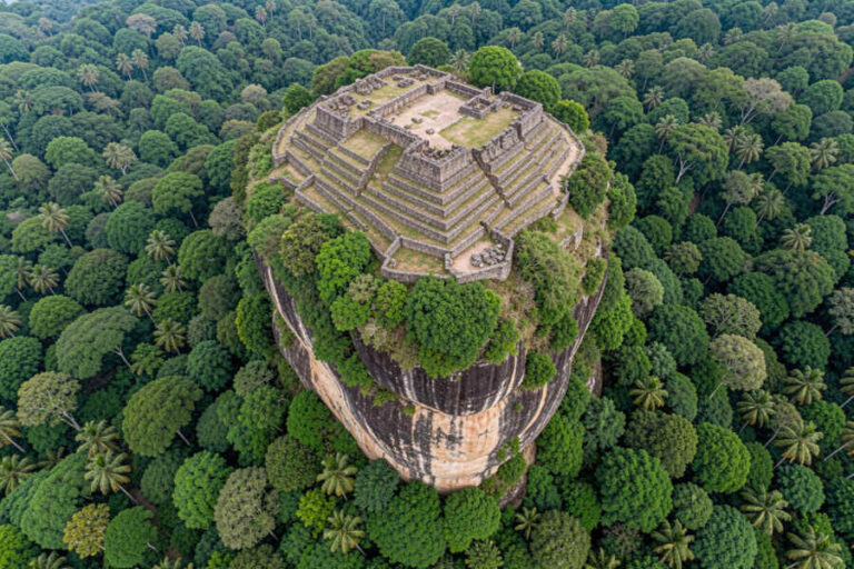 Aerial view of Sigiriya Rock Fortress: a stepped stone citadel atop a tall, forest-covered rock in Sri Lanka.