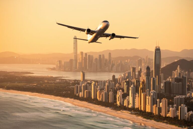 Airplane taking off over a coastal city skyline at sunset, with tall buildings along the shore.