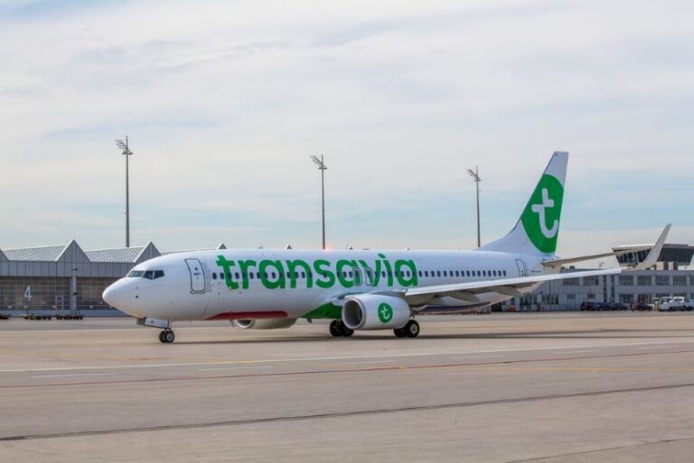 Transavia passenger jet parked on the tarmac beside a terminal at the airport, branding in green on white fuselage and tail.