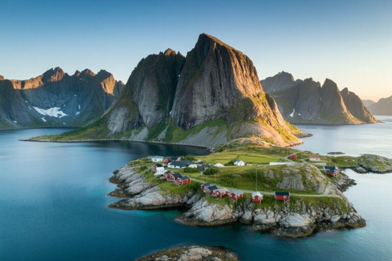 Aerial view of a rocky island with red houses along the shore and towering mountains in the background.
