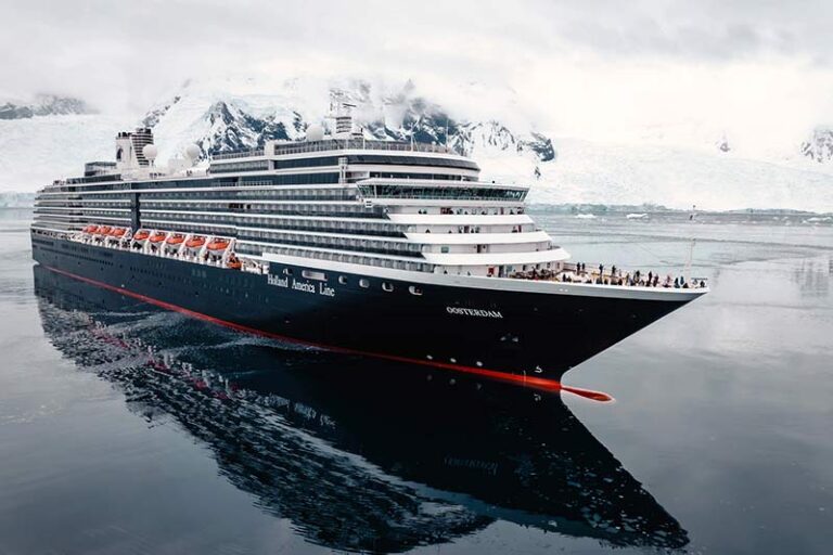 Large cruise ship sailing through icy water with snow-covered mountains in the background near a polar landscape.
