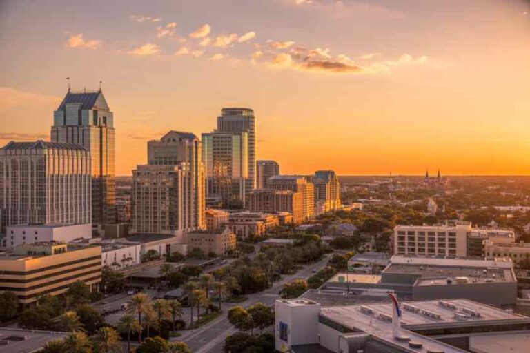 Downtown skyline at sunset with tall glass buildings bathed in orange light to the horizon.