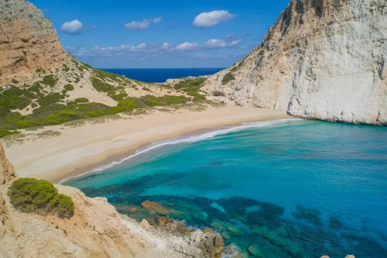 Turquoise cove with a sandy beach bordered by tall white cliffs and clear blue water under a sunny sky