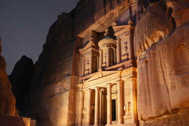 Ancient carved temple facade with columns in a sandstone cliff, illuminated at night in Petra-like scenery.