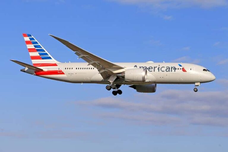 American Airlines jet in flight with landing gear extended against a blue sky.