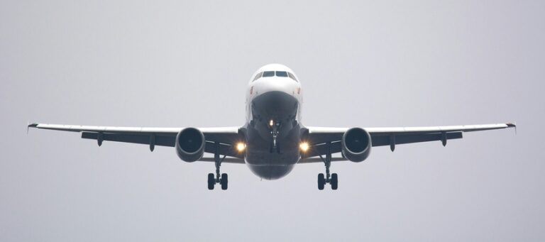 Front view of a commercial airliner approaching to land with landing gear down and runway headlights visible amid a gray sky.