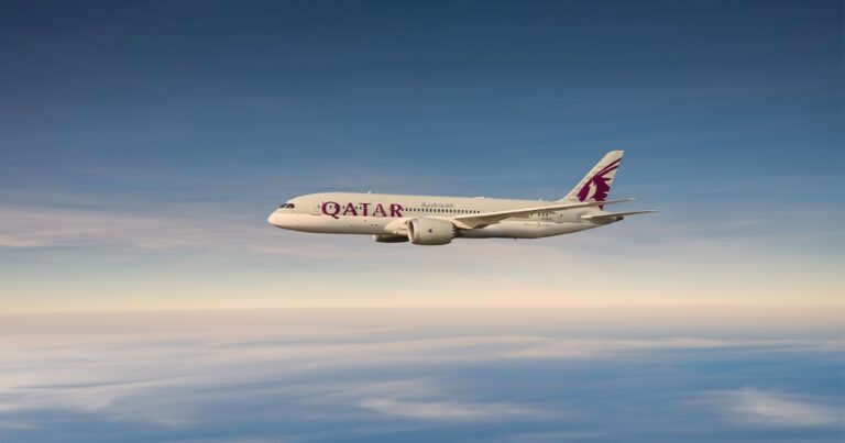 Qatar Airways passenger jet flying above a blue sky with clouds below.