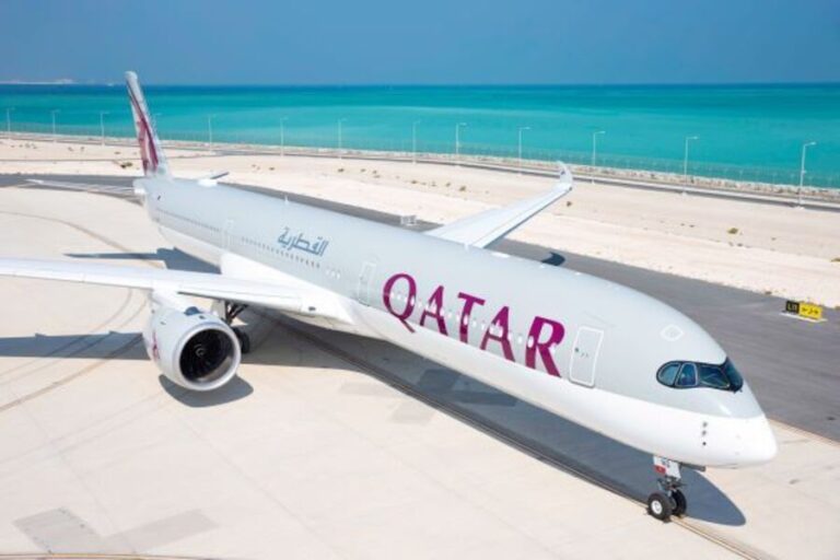 Qatar Airways widebody aircraft parked on a sunny airport ramp with a turquoise sea in the background