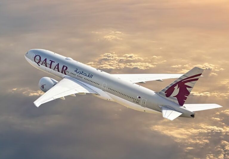 Qatar Airways passenger jet climbs above orange clouds at sunset.