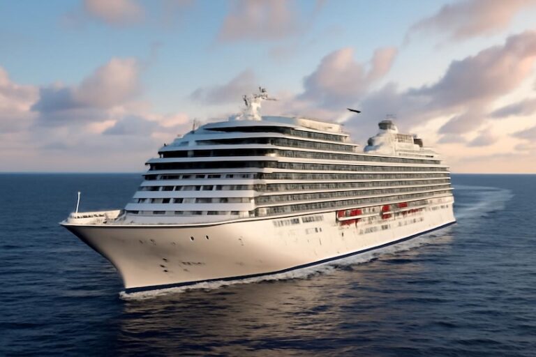 White cruise ship sailing on calm blue sea at sunset with pink-tinged clouds nearby as it moves forward