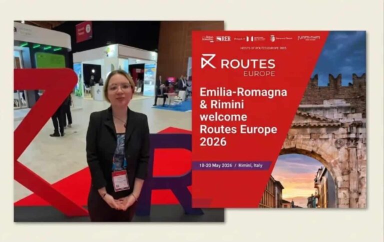 Woman in business attire standing at a Routes Europe 2026 booth, Emilia-Romagna & Rimini welcome banner in the background.