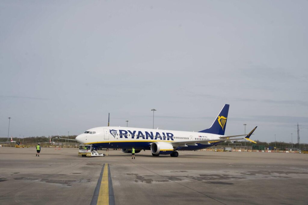 Ryanair jet on the tarmac with ground crew guiding it during pre-flight operations.