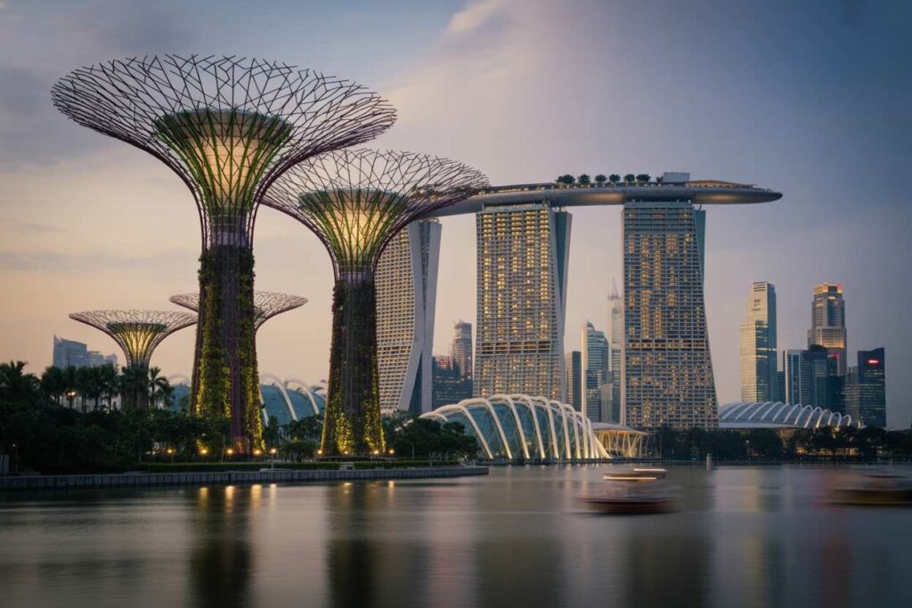 Nighttime view of Marina Bay skyline with illuminated Supertrees along the water and the Marina Bay Sands hotel in the distance.