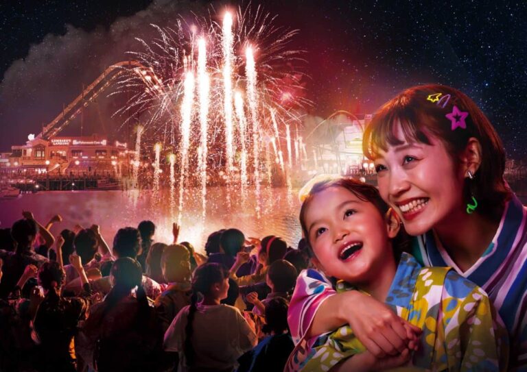 Mother and child in colorful yukatas smile as fireworks light a festival crowd behind them at night fall.