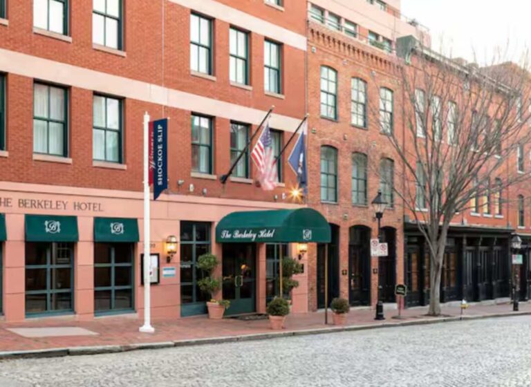 Brick hotel façade on a cobblestone street with a green entrance awning and flags above the door.