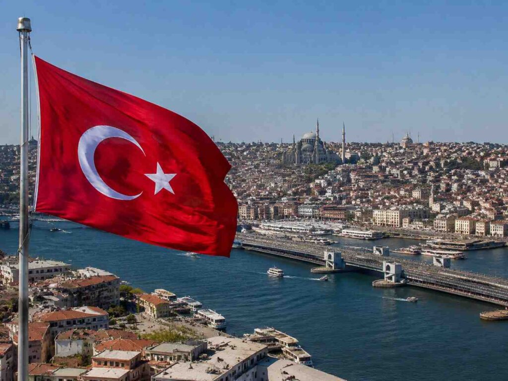 Turkish flag waving in the wind with Istanbul's skyline and the Bosphorus Strait in the background.
