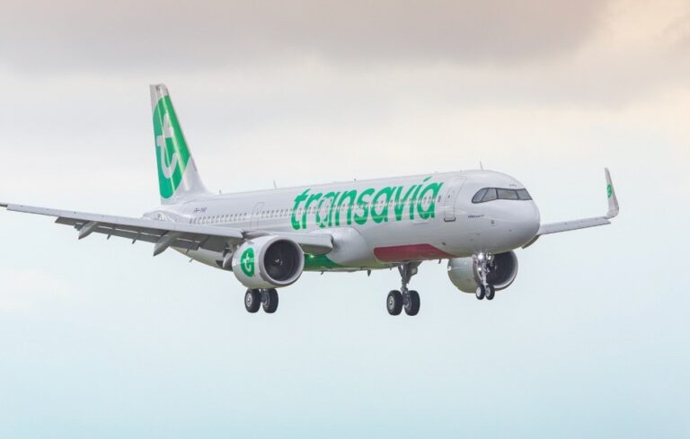Airplane in flight with green Transavia branding approaching for landing, landing gear down and extended