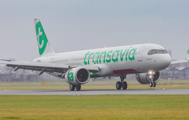 Transavia aircraft taxiing on a runway with green logo on the white fuselage under an overcast sky.
