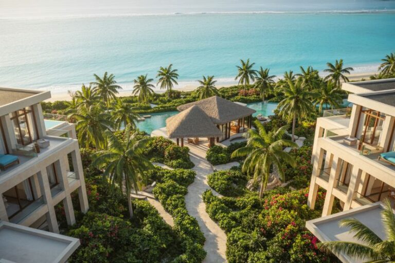 Overhead view of a luxury beachfront resort: palm trees, a thatched gazebo, two modern villas, and a turquoise sea beyond.