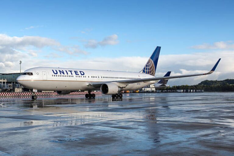 United Airlines wide-body aircraft on a wet airport tarmac with blue sky and clouds in the background