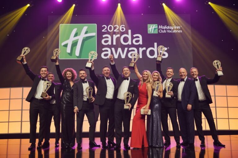 Group of people in formal attire on stage, holding trophies at the 2026 ARDA Awards ceremony with a bright backdrop and spotlights.