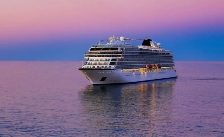 White cruise ship gliding on calm sea at sunset with pink and purple sky.