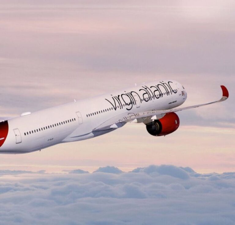 Virgin Atlantic airplane mid-flight above a sea of clouds at sunset, red engine cowling visible