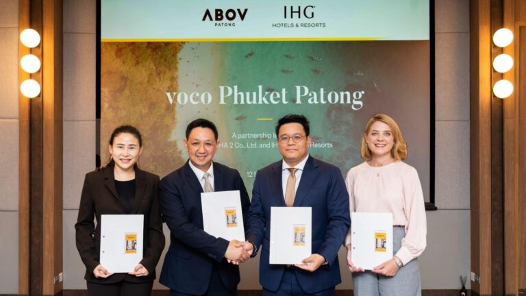 Four professionals in business attire pose on stage, holding folders as two men shake hands during a signing event; backdrop shows 'voco Phuket Patong' and partner logos.