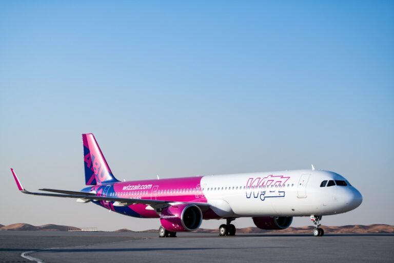 Pink and white Wizz Air Airbus A320 on a runway against a clear blue sky in a desert setting.