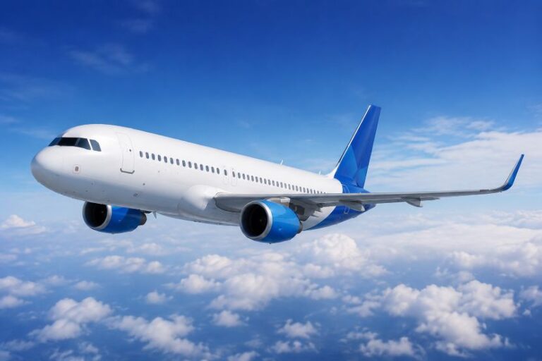 White commercial airplane with blue engines and tail flying above a sea of clouds in clear blue sky.