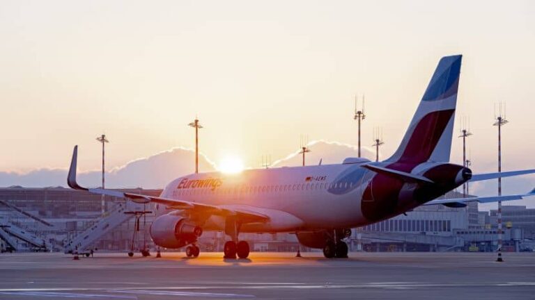 Sunset over a Eurowings passenger plane parked on the airport tarmac with ground equipment nearby.