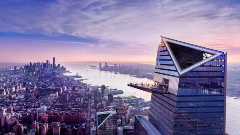 Aerial view of New York City at sunset, with a futuristic glass skyscraper featuring a protruding observation deck over the skyline and river.