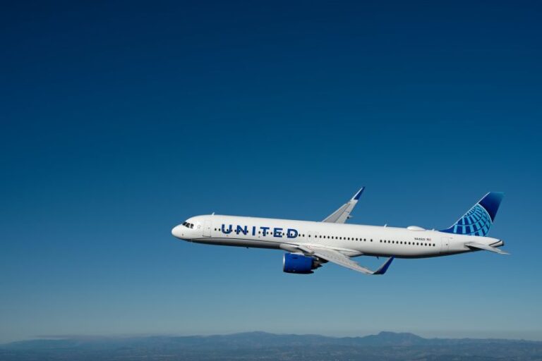 White United Airlines jet in flight against a clear blue sky with mountains below, branding visible on fuselage and tail