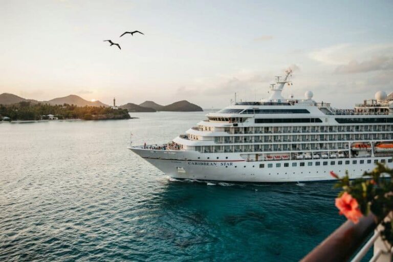 A large white cruise ship named Caribbean Star on turquoise water near a tropical coastline at sunset.