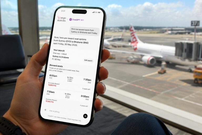 Close-up of a hand holding an iPhone showing a flight booking chat with Virgin Australia at an airport terminal window view behind.