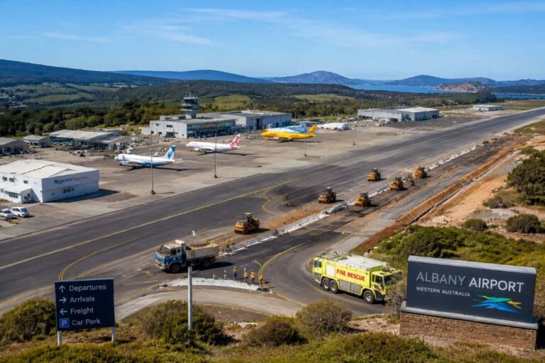 Albany Airport in Western Australia with construction on the runway; multiple planes parked near the terminal, a control tower in the background, and construction vehicles along the taxiway.
