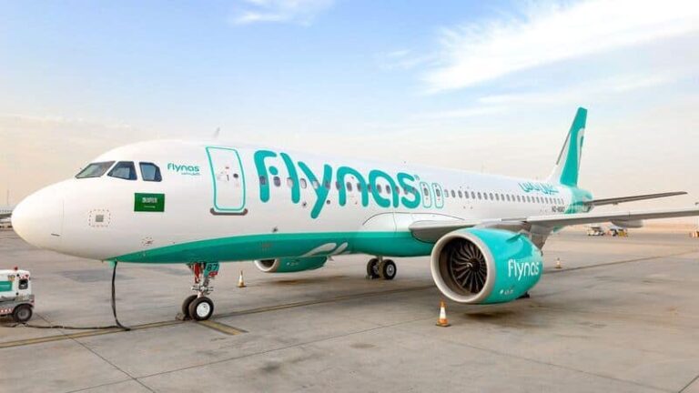 White and turquoise Flynas airplane on the tarmac with engines visible and ground crew nearby at an airport.