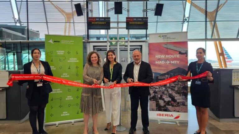 Six people stand in a bright airport terminal cutting a red ribbon to celebrate a new Iberia route MAD-MTY via Monterrey, with banners in the background.