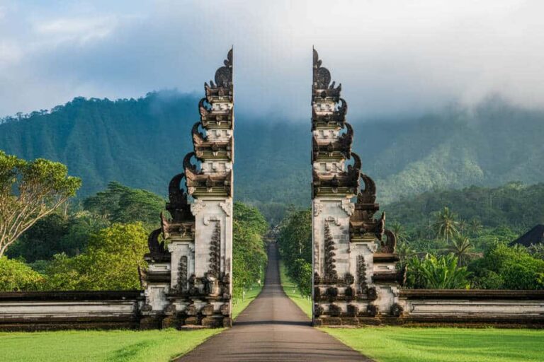 Twin ornate temple gates framing a straight road through a lush tropical valley with distant mountains under a cloudy sky.