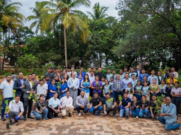 Group of people posing outdoors with small saplings, likely a tree-planting or environmental event in a park.