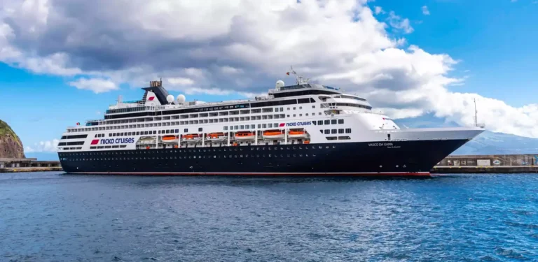 Large cruise ship Nicko Cruises Vasco da Gama docked at a harbor, blue water and cloudy sky in the background