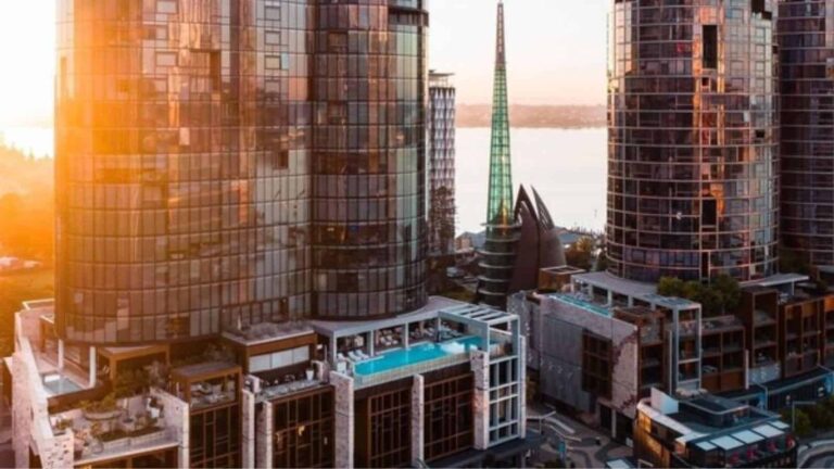 Sunlit urban skyline with glass skyscrapers and a rooftop pool in the foreground.”,