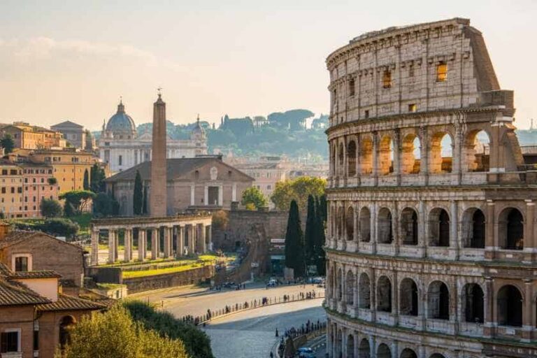 Historic Rome: the Colosseum with ancient ruins and a curved roadway under a warm sunset sky.