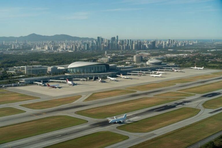 Aerial view of a large airport with multiple airplanes on runways and a city skyline in the background.