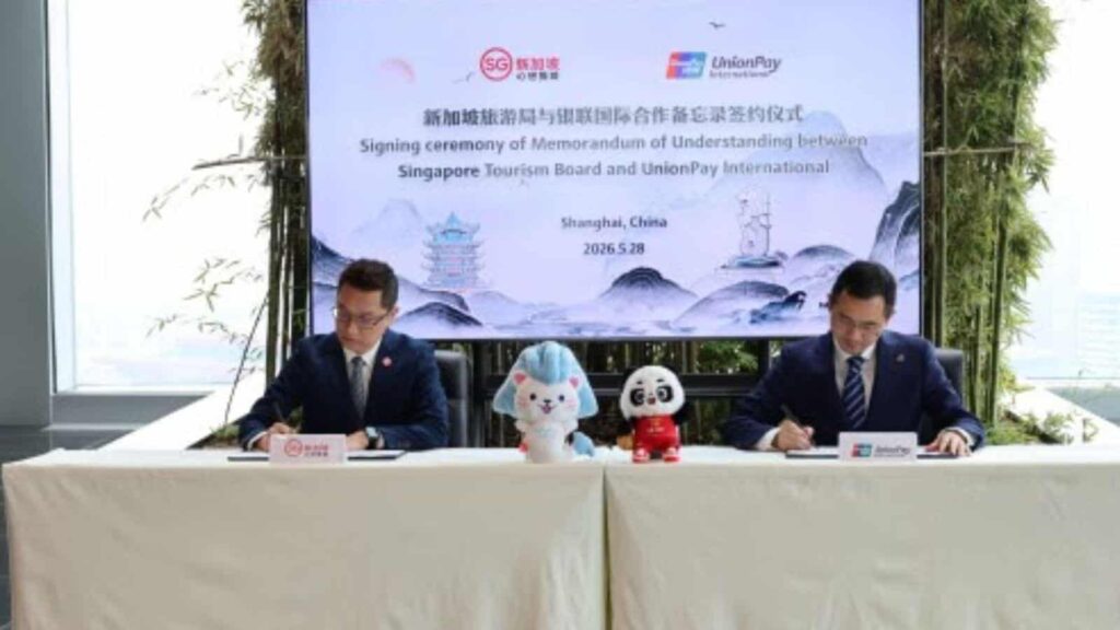 Two men in suits sign documents at a formal ceremony table, with blue bunny and panda mascots between them and a banner in the background.