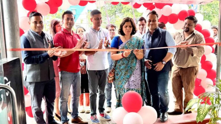Group of people at a ribbon-cutting ceremony with red and white balloons in the background.