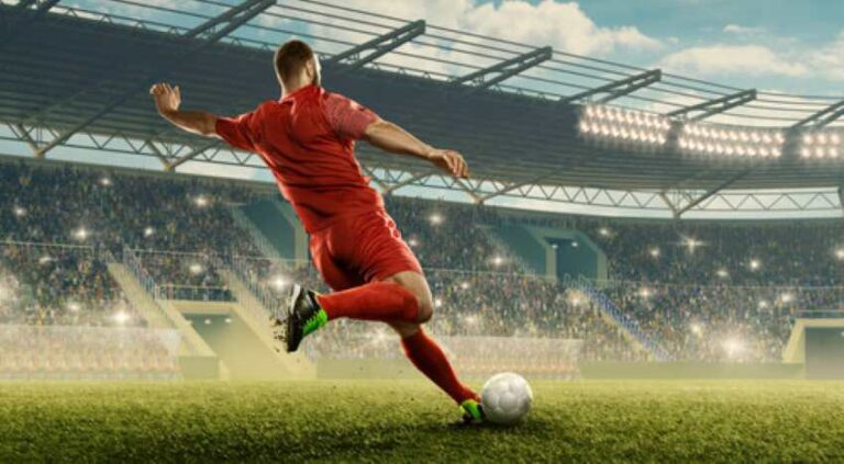 Soccer player in red kicking a ball on a crowded stadium field at night/under lights